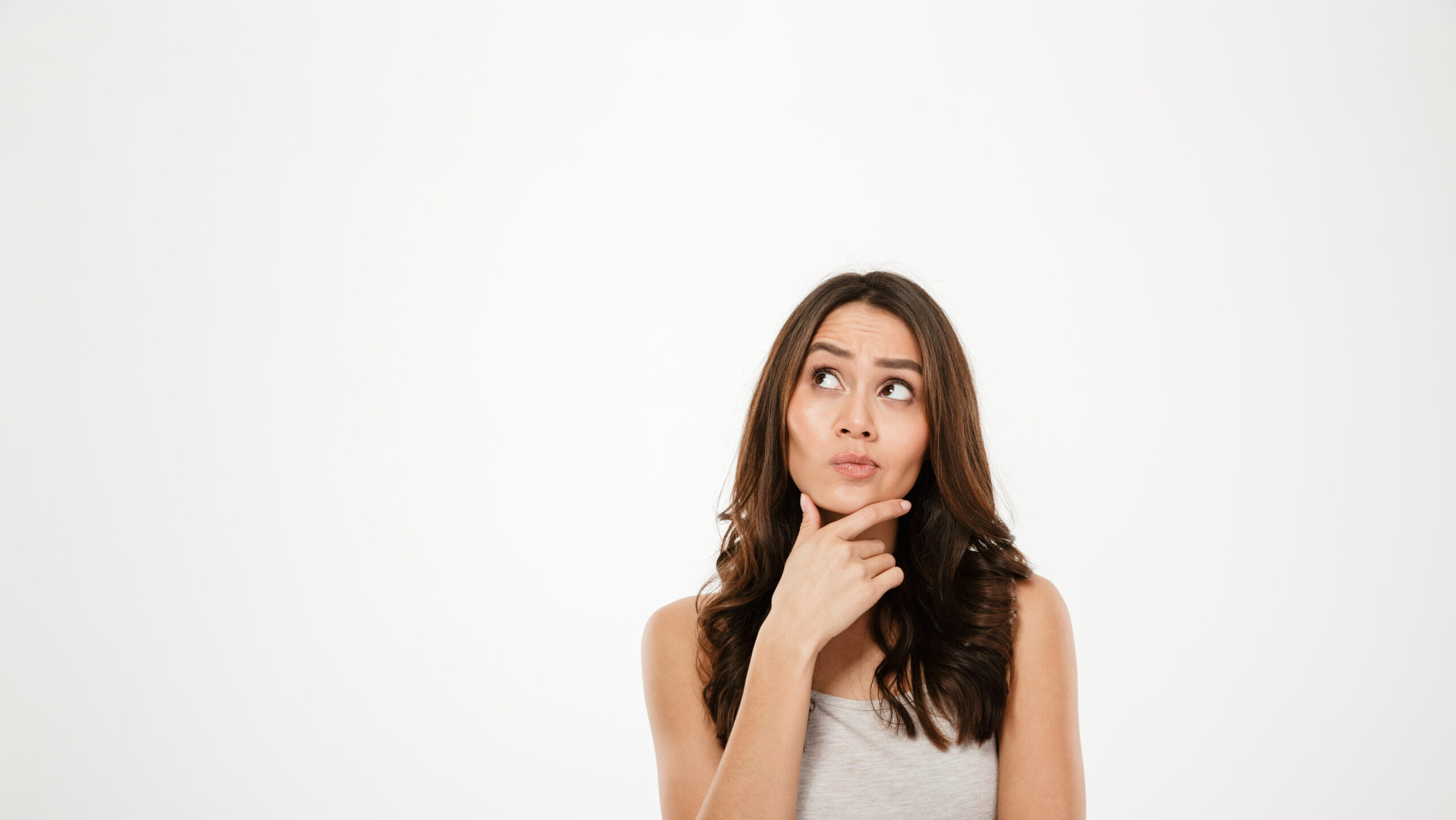 Image of Pensive brunette woman holding her chin and looking up over gray background